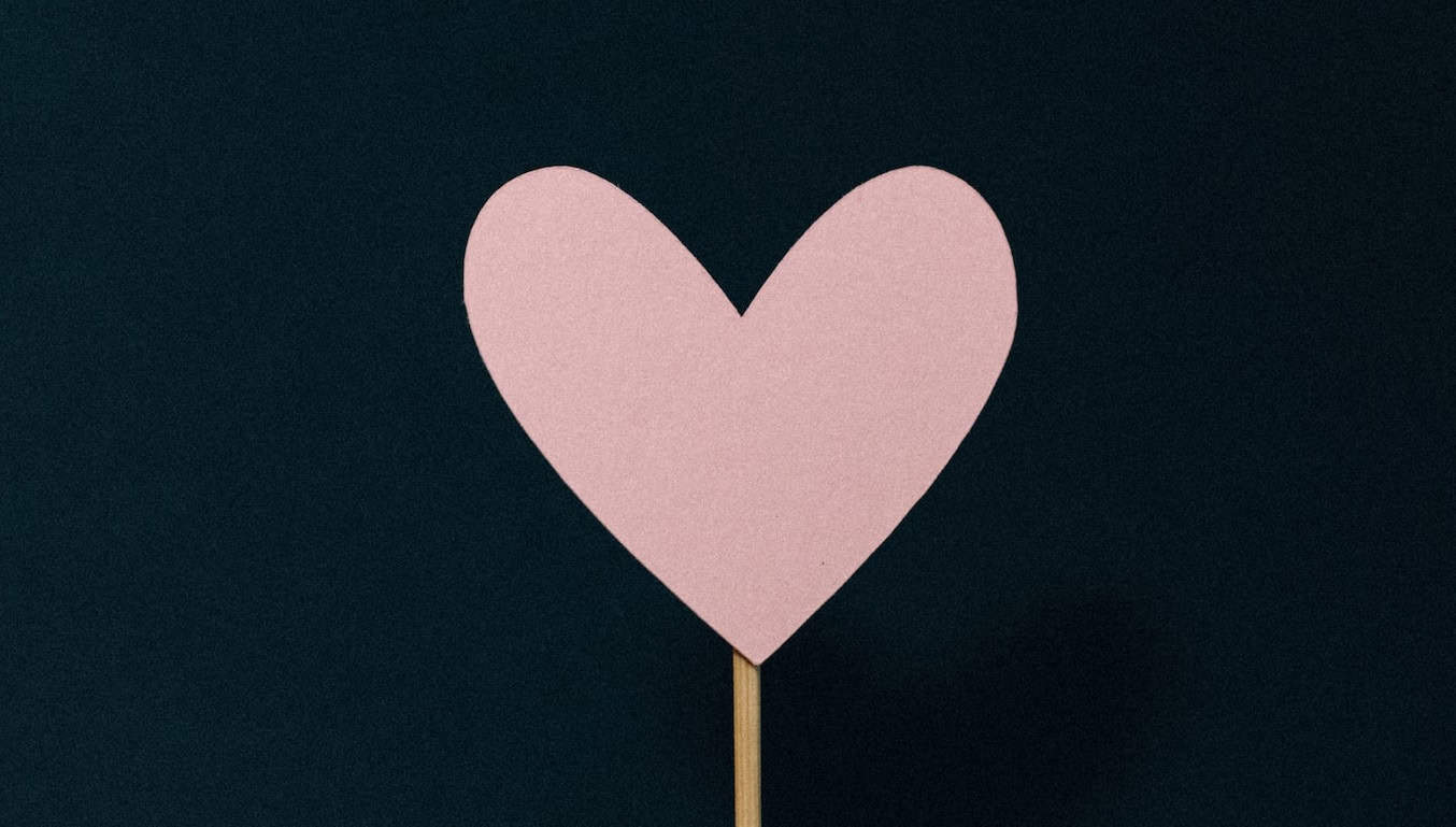 |a paper pink heart stuck onto a stick on a black background