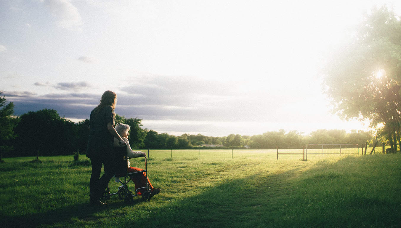 carer-pushing-elderly-woman-in-wheelchair-countryside