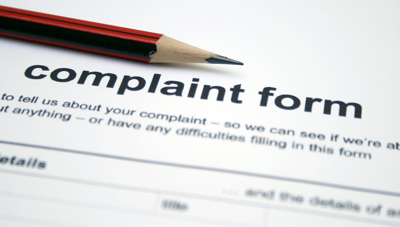 A red sharpened pencil sits on the heading of a blank complaint form. The form has black text printed on white paper.