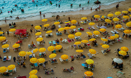 A vibrant aerial view of sunbathers and yellow umbrellas on a sandy beach
