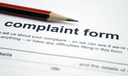 A red sharpened pencil sits on the heading of a blank complaint form. The form has black text printed on white paper.