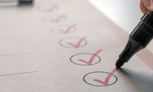 checklist with red ticks in circles and a person holding a pen