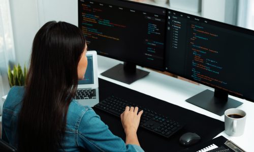 Young Asian in IT developer creating with typing online information on pc with coding program data of website application, wearing jeans shirt. surrounded by safety analysis two screens.